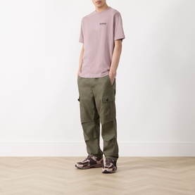 Model wearing Barbour Moonwell Graphic Logo T-Shirt in Ironstone pink, styled with olive green cargo trousers and purple chunky trainers.
