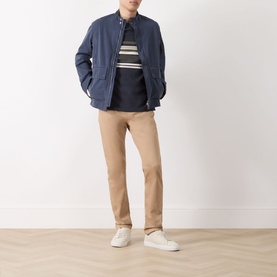Model wearing Barbour Teeside Graphic Logo T-Shirt in Dark Navy with stripe detail, styled with navy jacket, beige trousers and white trainers.