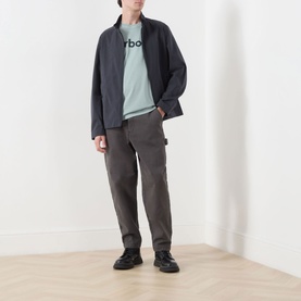 Model wearing Barbour Washington Overdyed Logo T-Shirt in Dusty Slate, styled with dark zip jacket, grey cargo trousers and black shoes.