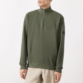 Model wearing Barbour International Thyme half-zip sweatshirt in olive cotton, with small arm badge detail, styled with stone chinos.