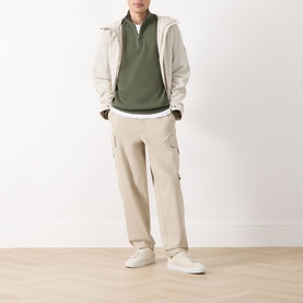 Model wearing Barbour International Thyme half-zip sweatshirt with beige cargo trousers, light jacket and white trainers.