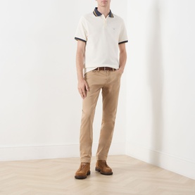 Model wearing Barbour Anthorn Textured Logo Polo Shirt in Whisper White with navy tipped collar, styled with beige chinos and brown leather shoes.