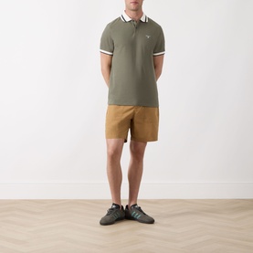 Model wearing Barbour Anthorn Textured Logo Polo Shirt in Dusty Olive with tan shorts and dark trainers.