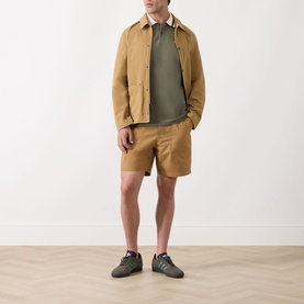 Model wearing Barbour Anthorn Textured Logo Polo Shirt in Dusty Olive, styled with tan jacket, matching shorts and grey trainers.