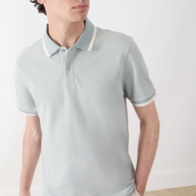 Model wearing Barbour Barnard Logo Polo Shirt in Dusty Slate, featuring contrast tipped collar, short sleeves, and embroidered logo detail.