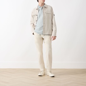 Model wearing Barbour Barnard Logo Polo Shirt in Dusty Slate, styled with cream overshirt, cream trousers and white trainers.