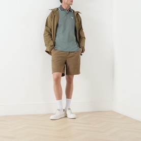 Model wearing Barbour Vintage Teal polo shirt, styled with tan jacket, matching shorts and white trainers.