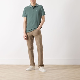 Model wearing Barbour Vintage Teal polo shirt with contrast tipping, styled with beige chinos and white trainers.