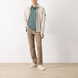 Model wearing Barbour polo in Vintage Teal, styled with a beige overshirt, tan trousers and white trainers.