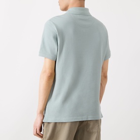 Model wearing Barbour polo shirt in Dusty Slate, short sleeves and textured fabric, styled with stone-coloured trousers, rear view.