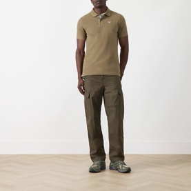 Model wearing Barbour clay cotton polo shirt, styled with dark olive cargo trousers and grey trail shoes.