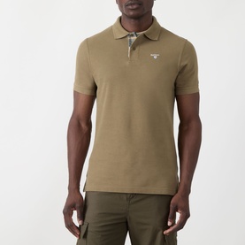 Model wearing Barbour polo shirt in Clay, short sleeves, white logo badge at chest, styled with khaki trousers
