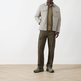 Model wearing Barbour clay cotton polo, styled with a light overshirt, olive cargo trousers, and green suede shoes.