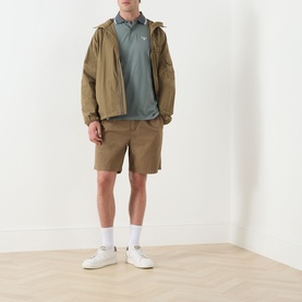 Model wearing Barbour clay cotton shorts, styled with a sage polo shirt, khaki jacket and white trainers.