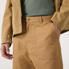 Model wearing Barbour Sherburn Logo Straight-Leg Shorts in camel, styled with a matching camel jacket and green T-shirt.