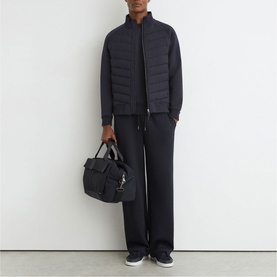 Model carrying a blue Reiss bag, styled with a navy quilted gilet, matching wide-leg trousers and dark trainers.