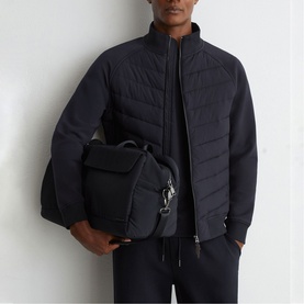 Model carrying Reiss blue bag with silver hardware, styled with a navy quilted jacket and dark trousers