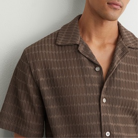 Model wearing Reiss taupe brown short-sleeve shirt with textured stripe pattern and open camp collar, styled open at the chest.