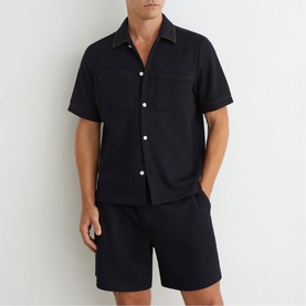 Model wearing Reiss blue short-sleeve shirt with chest pockets, styled with matching blue shorts