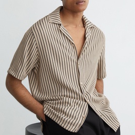 Model wearing Reiss beige stripe short-sleeve relaxed shirt with open collar, styled with black trousers.