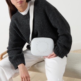 Model carrying Stella McCartney Logo Camera Crossbody Bag in Pearl Grey, silver-tone hardware, circular logo detail, worn crossbody over dark knit