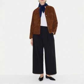 Model wearing a tan brown suede jacket with chest pockets, styled with white tee, navy neckerchief, wide-leg black trousers and black flats