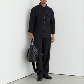 Model wearing Reiss blue overshirt and tailored trousers, carrying a black leather holdall, styled with black leather shoes.