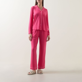 Model wearing Chelsea Peers Patch Pocket Long Pyjama Set in pink with contrast piping, paired with white slider sandals.