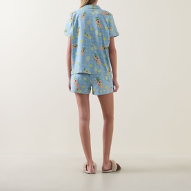 Model wearing Chelsea Peers Tennis & Cocktails Short Pyjama Set in blue with allover print, shown from behind, styled with nude slider sandals.