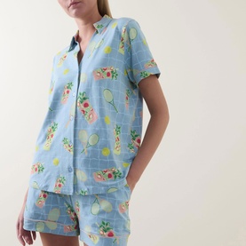 Model wearing Chelsea Peers Tennis & Cocktails Short Pyjama Set in blue with floral and tennis print, collared short-sleeve top and matching shorts.