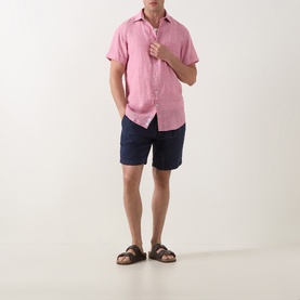 Model wearing Rodd & Gunn pink short-sleeve linen shirt, styled with navy shorts and brown leather sandals.