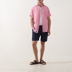 Model wearing Rodd & Gunn pink short-sleeve casual shirt, styled with navy shorts and brown sandals.