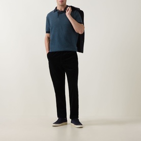 Model wearing Rodd & Gunn Oyster Island Striped Knitted Polo Shirt in teal, styled with black trousers and navy shoes, jacket over shoulder.