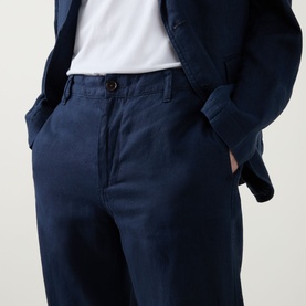 Model wearing Rodd & Gunn Spencer Bay Linen Trousers in navy, styled with a white tee and navy blazer, hands in side pockets.