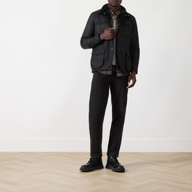 Model wearing Barbour black wax cotton casual jacket, styled with plaid shirt, dark trousers, and black chunky sole shoes.