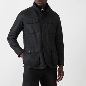 Model wearing Barbour black wax cotton casual jacket with button front, funnel collar, and multiple chest and hip pockets.