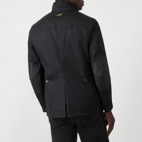 Model wearing Barbour black wax cotton casual jacket, rear view, with contrasting dark leather-look sleeve panels and gold logo badge.