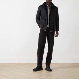 Model wearing Barbour black wax cotton casual jacket, styled with check shirt, dark trousers and black lace-up boots.