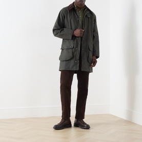 Model wearing Barbour green waxed cotton casual jacket with corduroy collar, styled with dark brown trousers and leather derby shoes