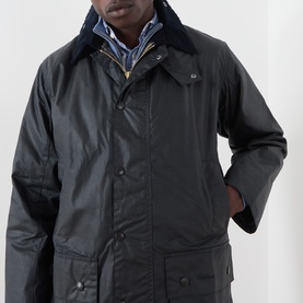 Model wearing Barbour navy waxed cotton casual jacket with corduroy collar, styled over a checked shirt with navy inner collar visible.