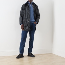 Model wearing Barbour navy waxed cotton casual jacket, styled with blue knitwear, checked shirt, dark jeans and black boots.