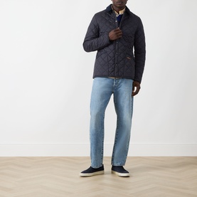 Model wearing Barbour navy quilted casual jacket, styled with light wash jeans and navy trainers