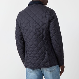 Model wearing Barbour navy quilted casual jacket, rear view, styled with light blue jeans. Diamond quilting pattern with corduroy collar detail.