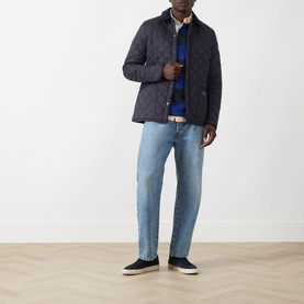 Model wearing Barbour navy quilted casual jacket, styled with blue knitwear, light-wash jeans and dark slip-on shoes.