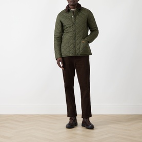 Model wearing Barbour Liddesdale Short Quilted Jacket in Olive with corduroy collar, styled with dark brown trousers and black leather shoes.