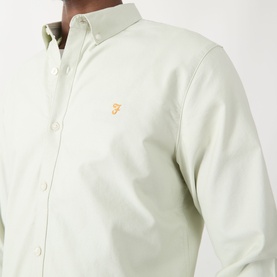 Model wearing Farah Vintage Brewer Logo Shirt in Soft Green, long-sleeve cotton with button-down collar and embroidered orange logo.