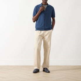 Model wearing Farah Vintage Poplar Knitted Polo Shirt in Aegean Blue, styled with cream trousers and a striped top underneath.