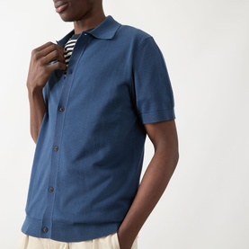 Model wearing Farah Vintage Poplar Knitted Polo Shirt in Aegean Blue, styled over a striped top with cream trousers