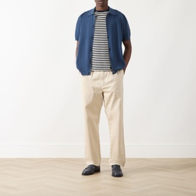 Model wearing Farah Vintage Poplar Knitted Polo Shirt in Aegean Blue, styled with striped tee, cream trousers and dark loafers.