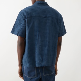 Model wearing Farah Vintage Olsen Textured Shirt in Aegean Blue, short-sleeve cotton seersucker, back view, styled with blue jeans.